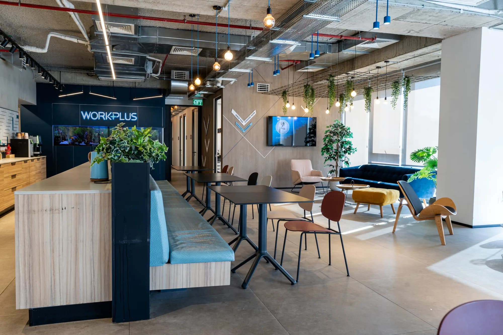 The WorkPlus coworking lounge: long wooden bar, teal banquette, hanging plants and the lit WorkPlus sign